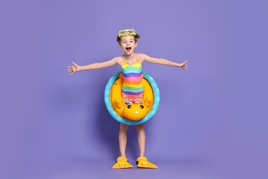 Happy girl in beachwear with diving mask, flippers and inflatable ring on purple background