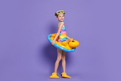 Photo of Happy girl in beachwear with diving mask, flippers and inflatable ring on purple background