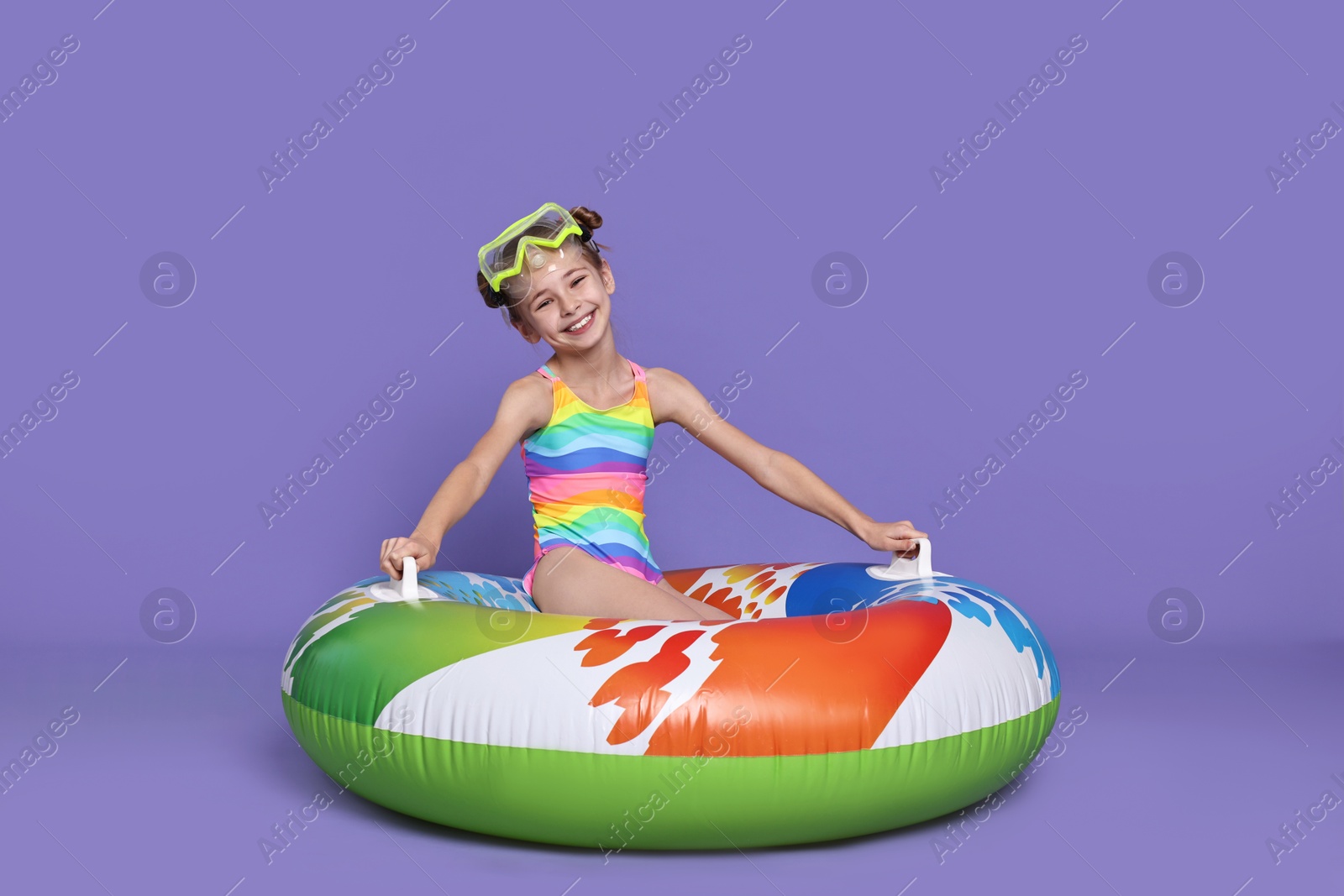 Photo of Happy girl in beachwear with diving mask and inflatable ring on purple background