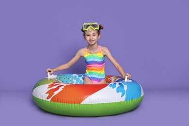 Photo of Happy girl in beachwear with diving mask and inflatable ring on purple background