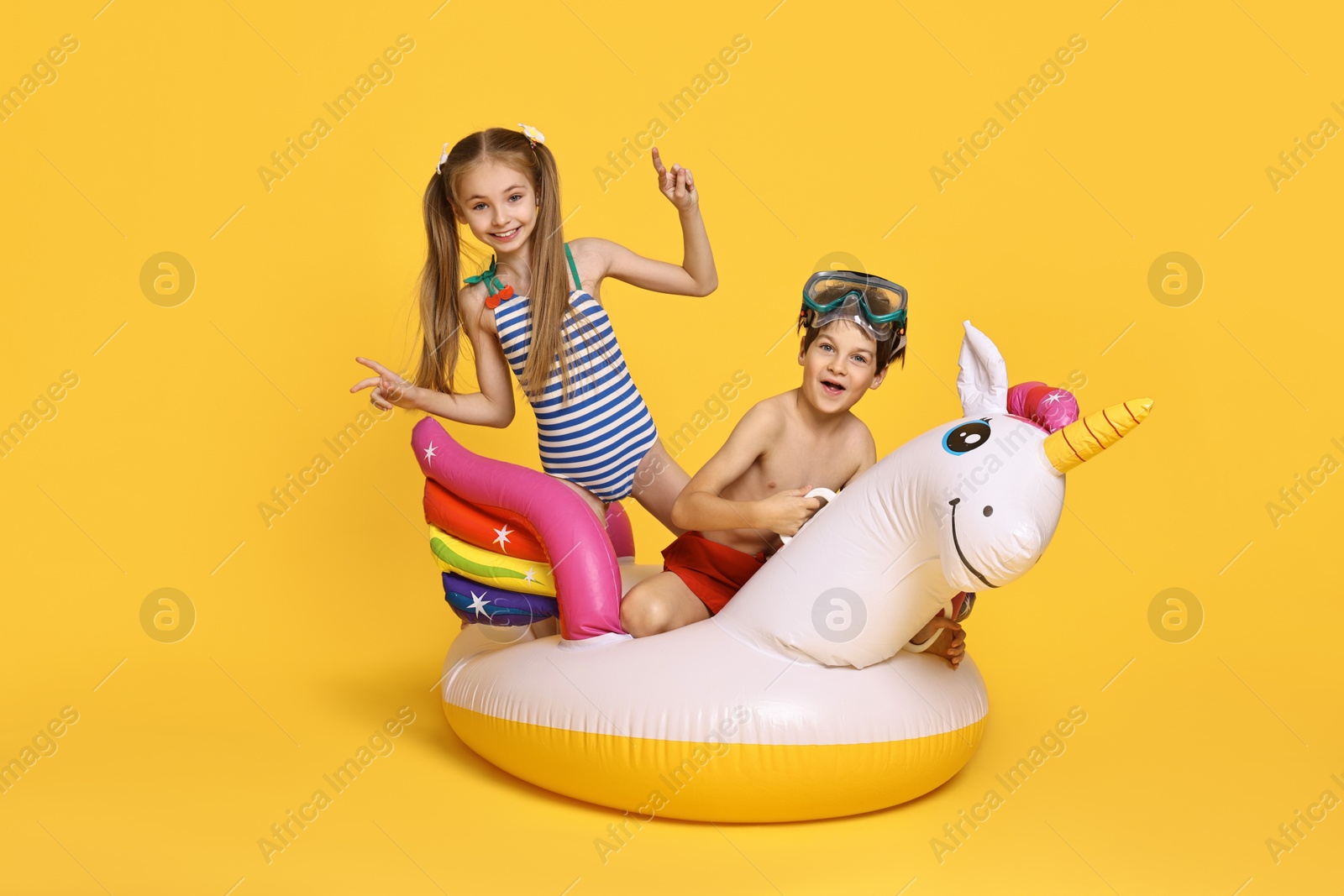 Photo of Happy little kids in beachwear with inflatable unicorn shaped ring on orange background