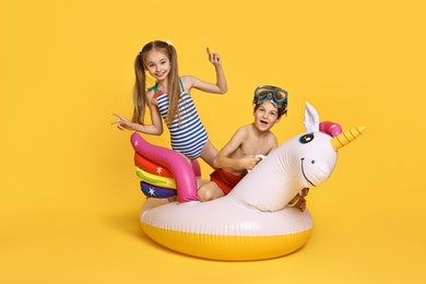 Photo of Happy little kids in beachwear with inflatable unicorn shaped ring on orange background