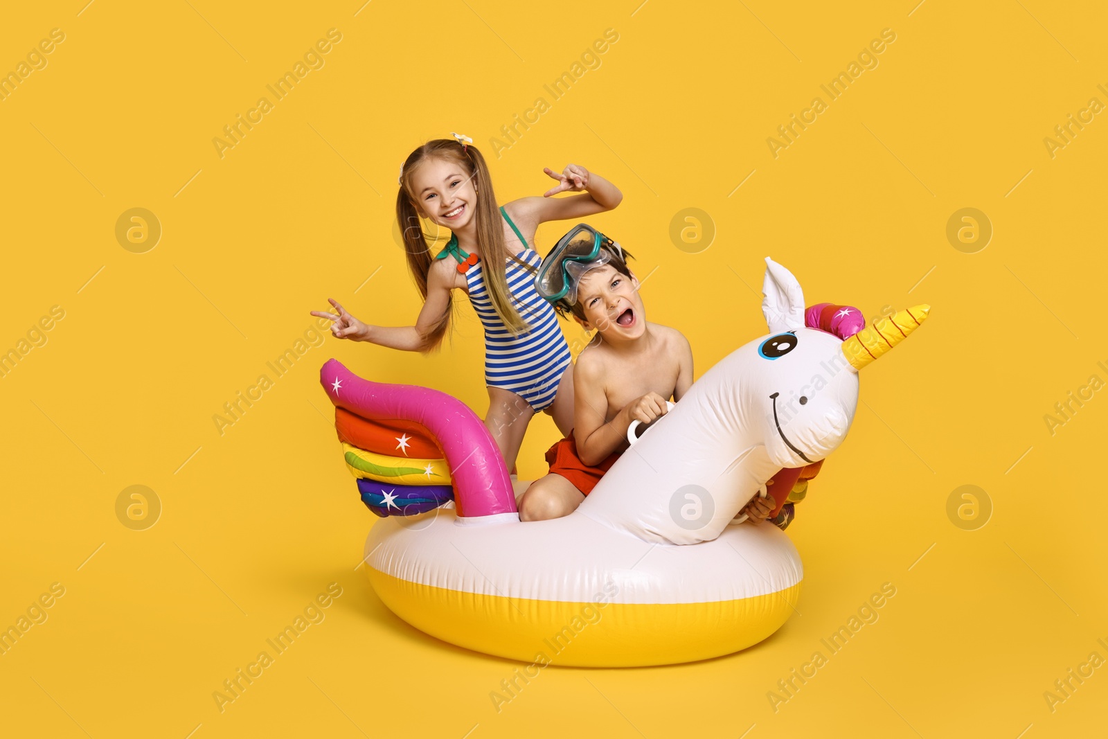 Photo of Happy little kids in beachwear with inflatable unicorn shaped ring on orange background