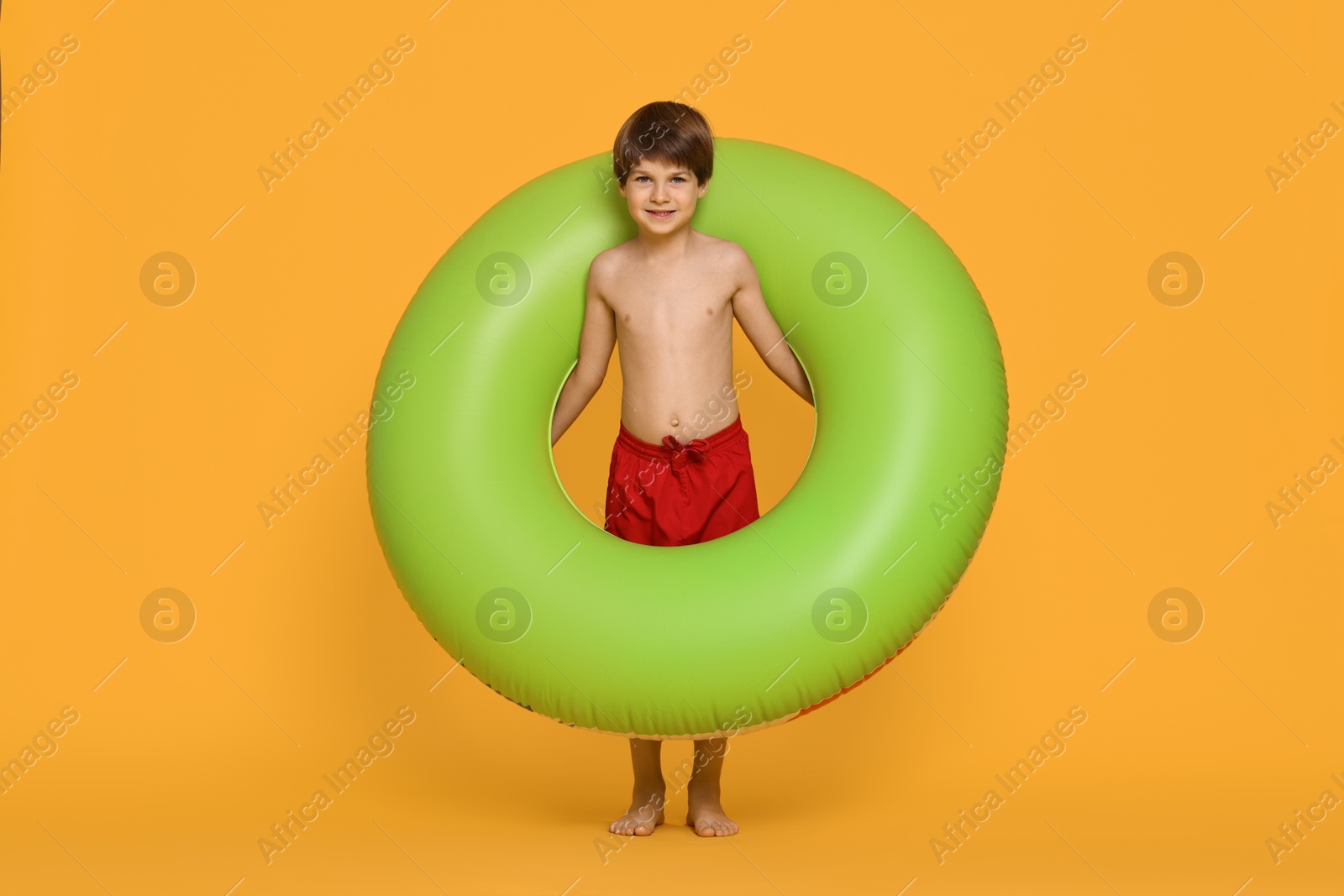 Photo of Little boy in beachwear with inflatable ring on orange background