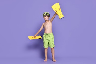 Little boy in beachwear with diving mask and flippers on purple background