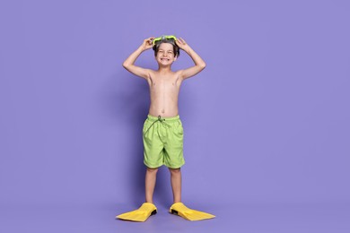 Photo of Little boy in beachwear with diving mask and flippers on purple background