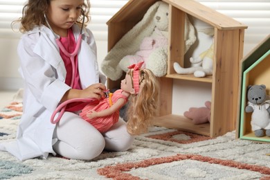 Photo of Cute little girl playing doctor with doll at home