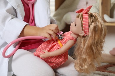 Photo of Little girl playing doctor with doll indoors, closeup