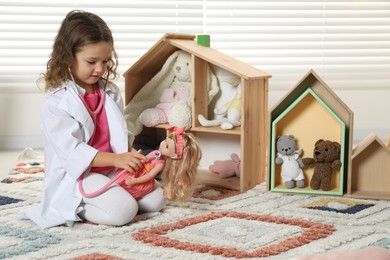 Photo of Cute little girl playing doctor with doll at home