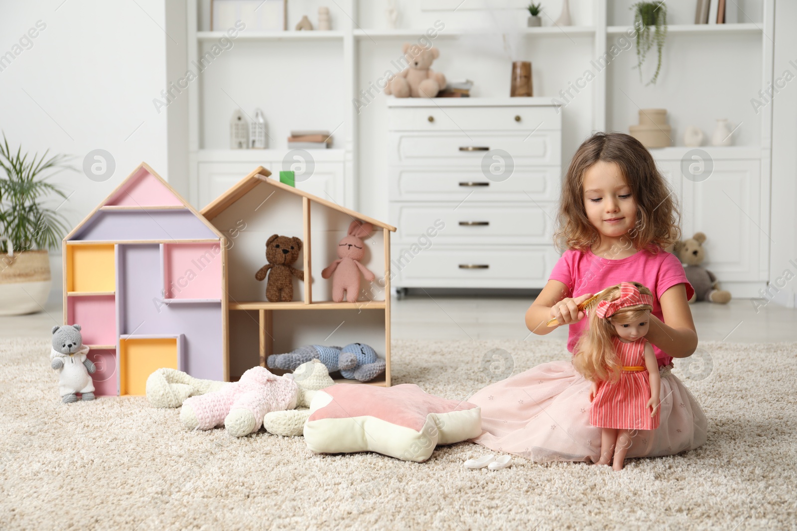 Photo of Cute little girl playing with doll and other toys on floor at home