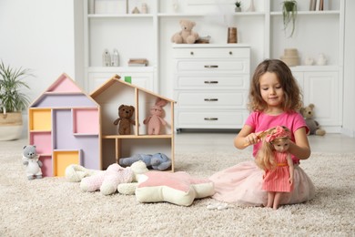 Photo of Cute little girl playing with doll and other toys on floor at home