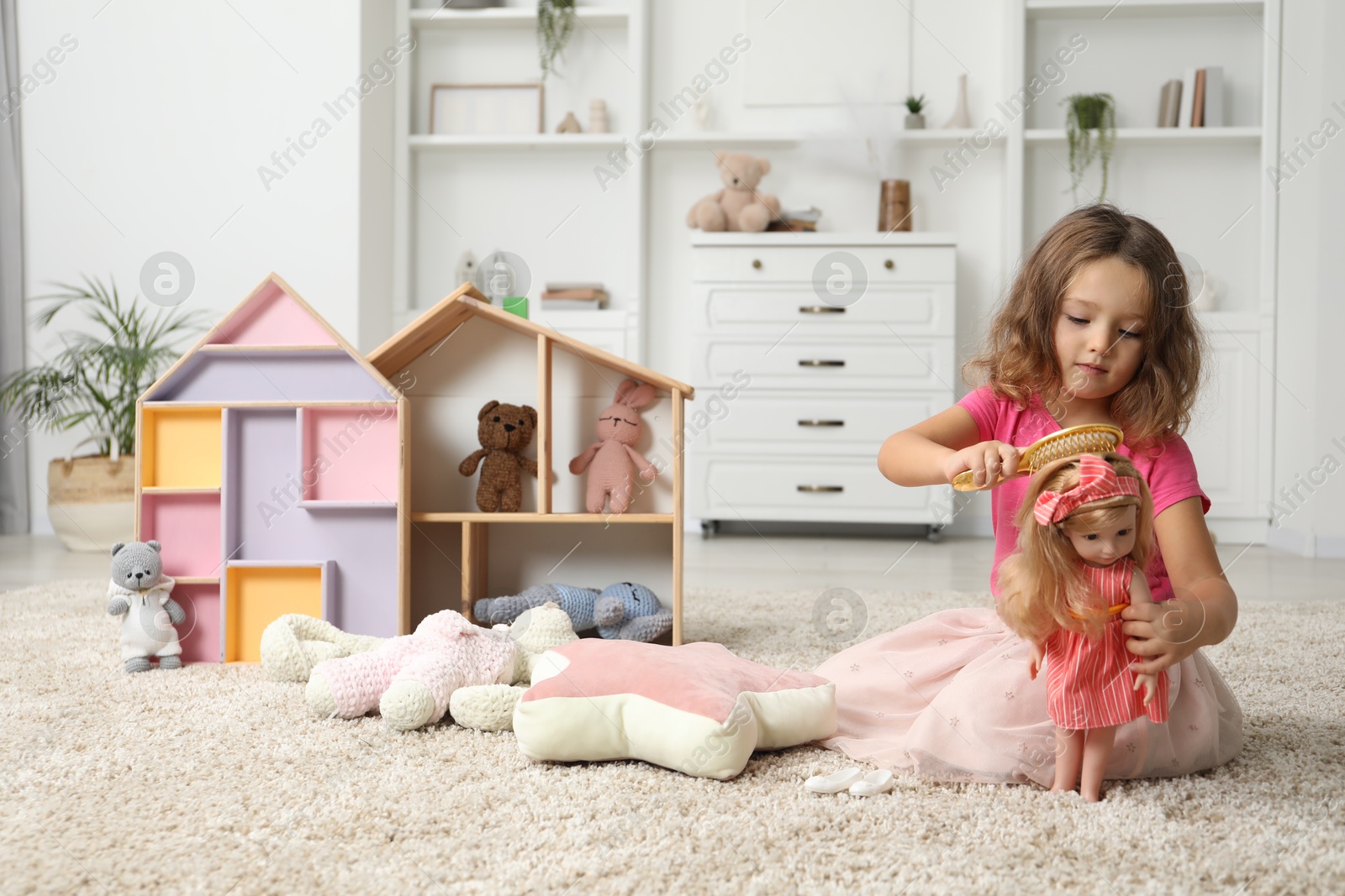 Photo of Cute little girl playing with doll and other toys on floor at home