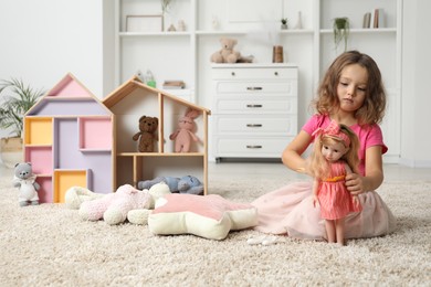 Photo of Cute little girl playing with doll and other toys on floor at home