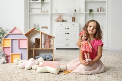 Photo of Cute little girl playing with doll and other toys on floor at home