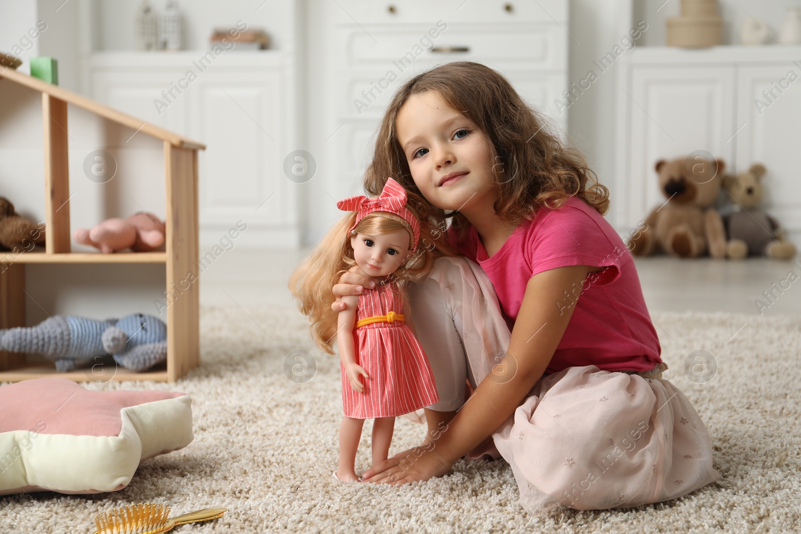 Photo of Cute little girl playing with her doll on floor at home