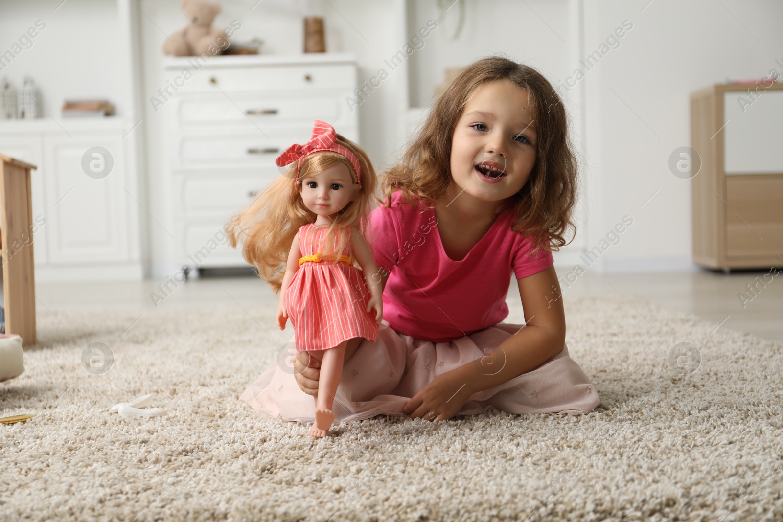 Photo of Cute little girl playing with her doll on floor at home