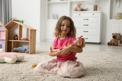 Photo of Cute little girl playing with her doll on floor at home