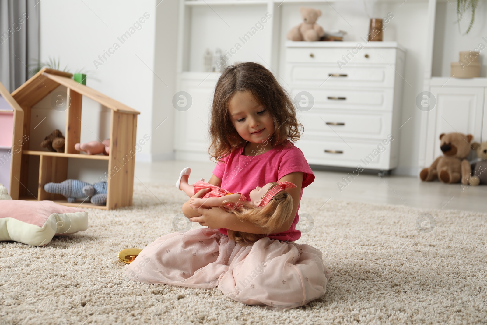 Photo of Cute little girl playing with her doll on floor at home