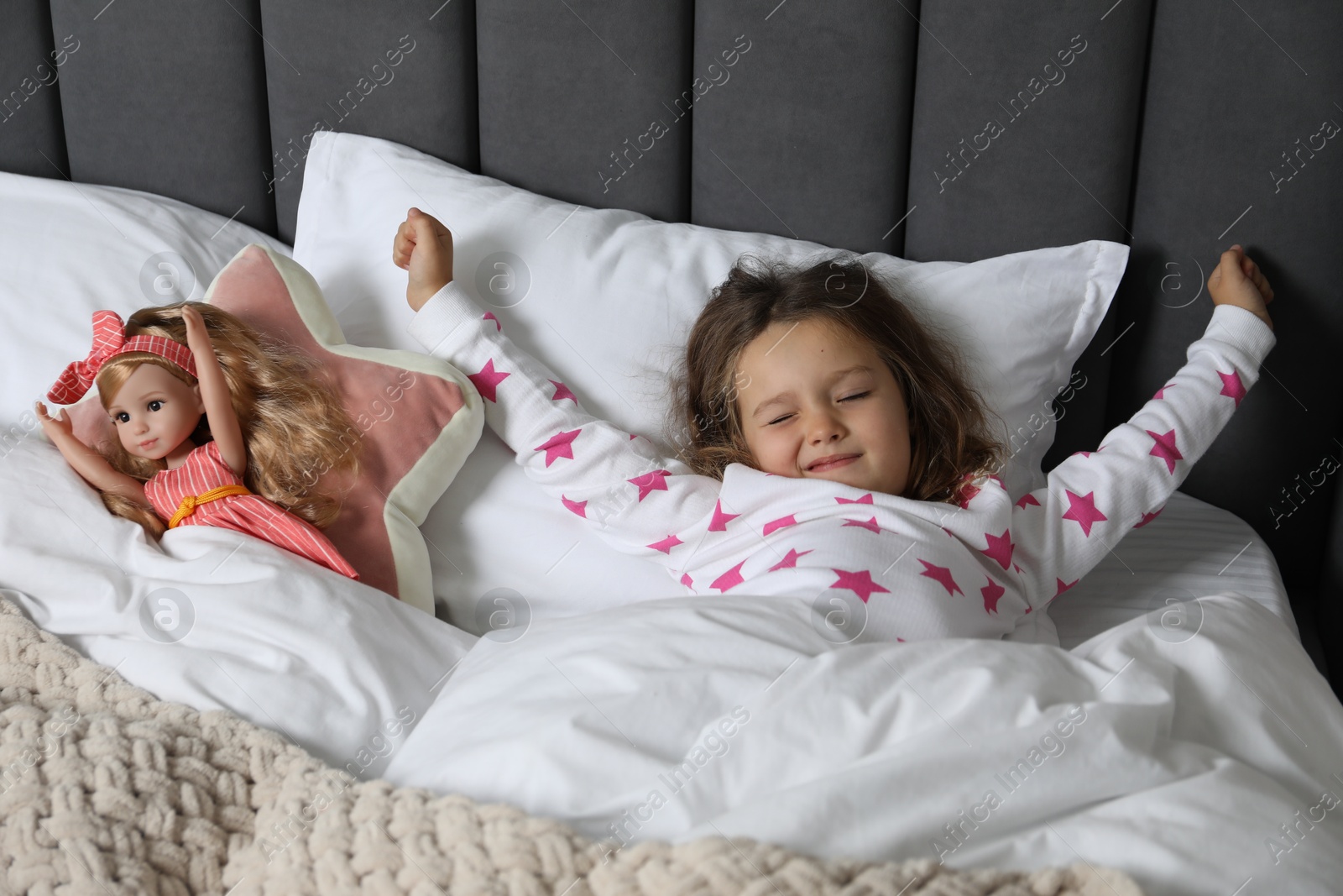 Photo of Cute little girl stretching near her doll in bed