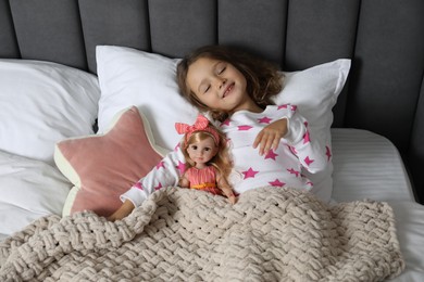 Photo of Cute little girl with doll under blanket in bed