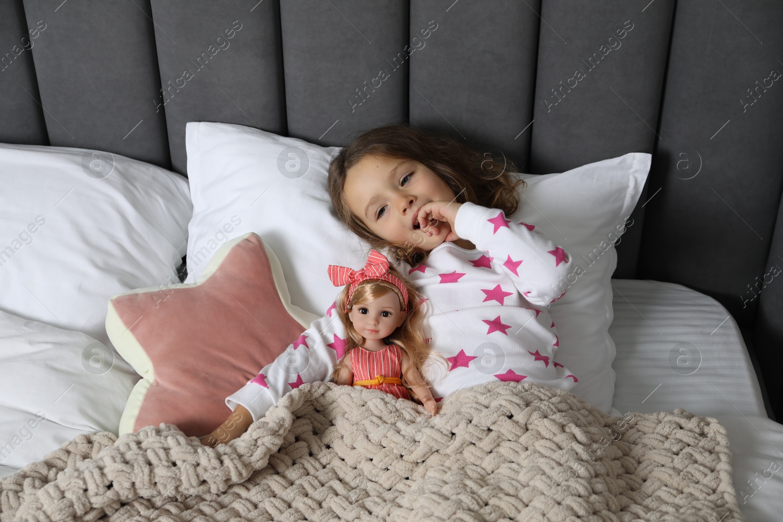 Photo of Cute little girl with doll under blanket in bed