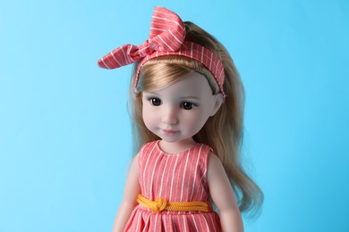 Photo of Beautiful doll in dress and headband on light blue background, closeup