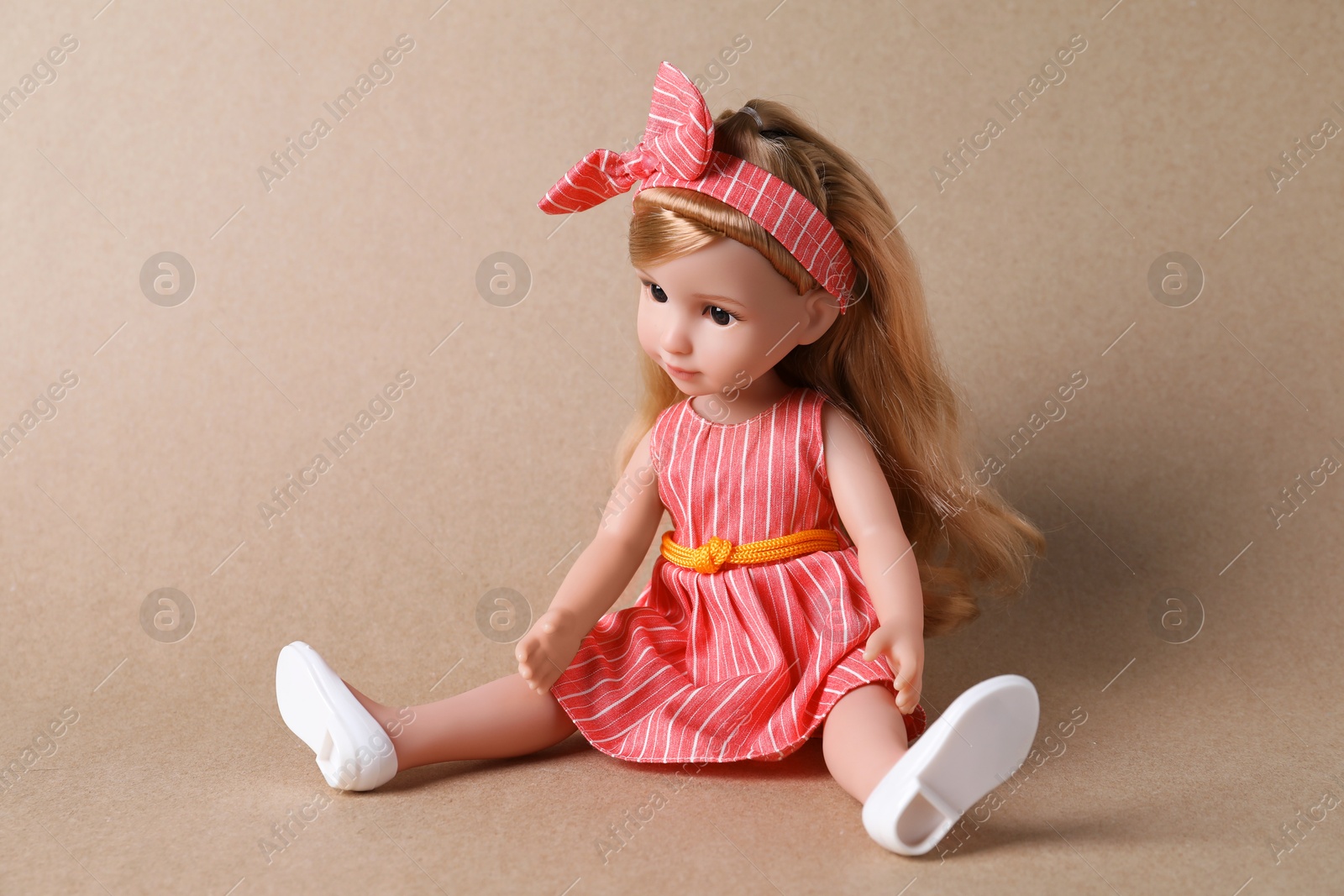 Photo of Beautiful doll in dress and headband on light brown background