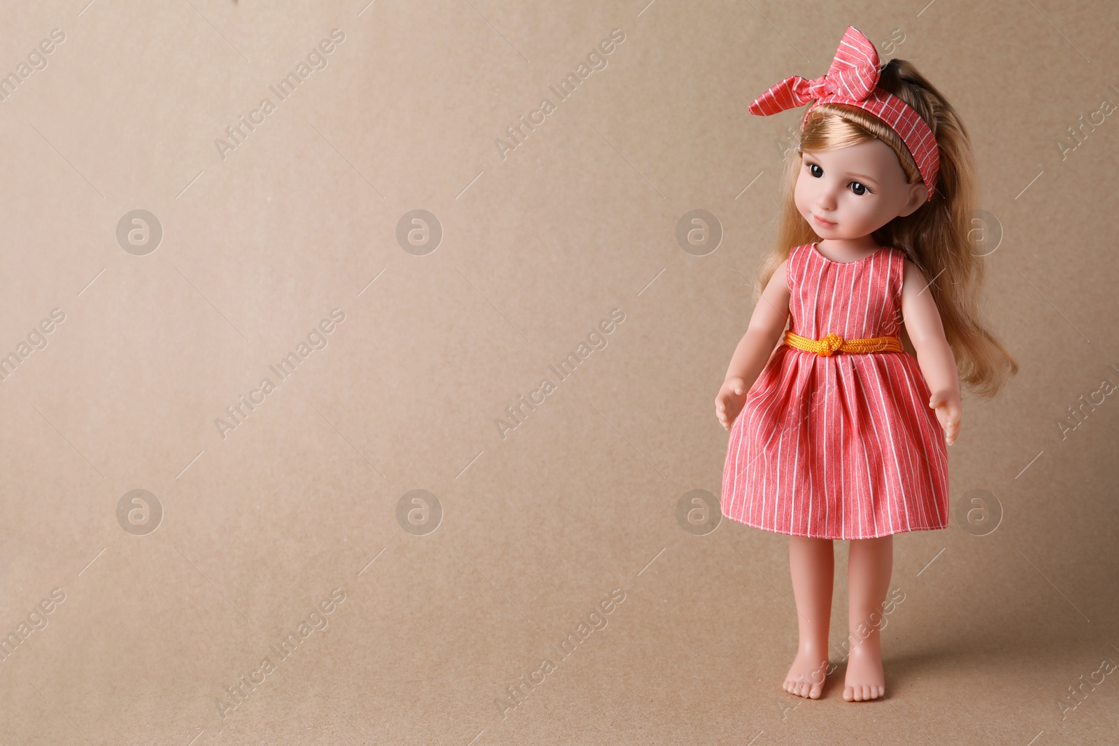 Photo of Beautiful doll in dress and headband on light brown background. Space for text