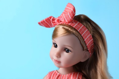 Photo of Beautiful doll with headband on light blue background, closeup. Space for text