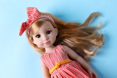 Photo of Beautiful doll in dress and headband on light blue background, top view