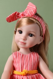 Beautiful doll in dress and headband on light green background, closeup