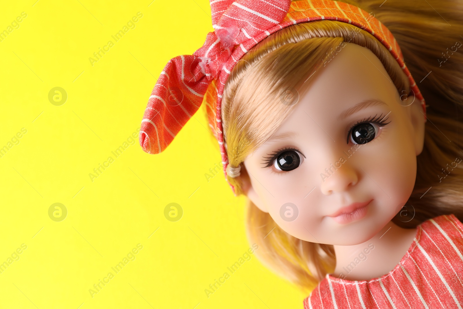 Photo of Beautiful doll in headband on yellow background, closeup. Space for text