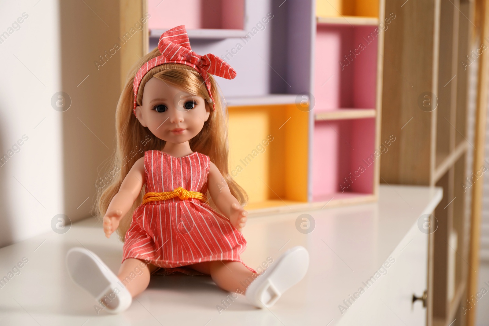 Photo of Beautiful doll in dress and headband on white table indoors, space for text