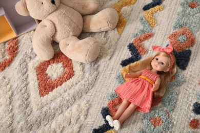 Photo of Beautiful doll in dress and teddy bear on soft carpet