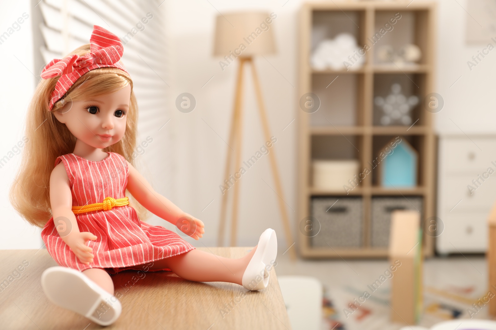 Photo of Beautiful doll in dress and headband on wooden table indoors, space for text