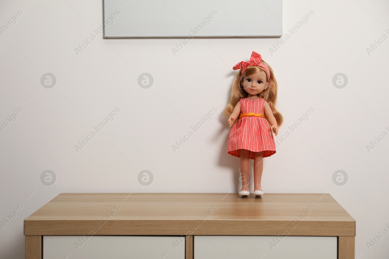 Photo of Beautiful doll in dress and headband on wooden table near white wall, space for text