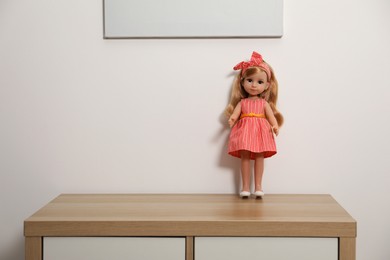 Photo of Beautiful doll in dress and headband on wooden table near white wall, space for text