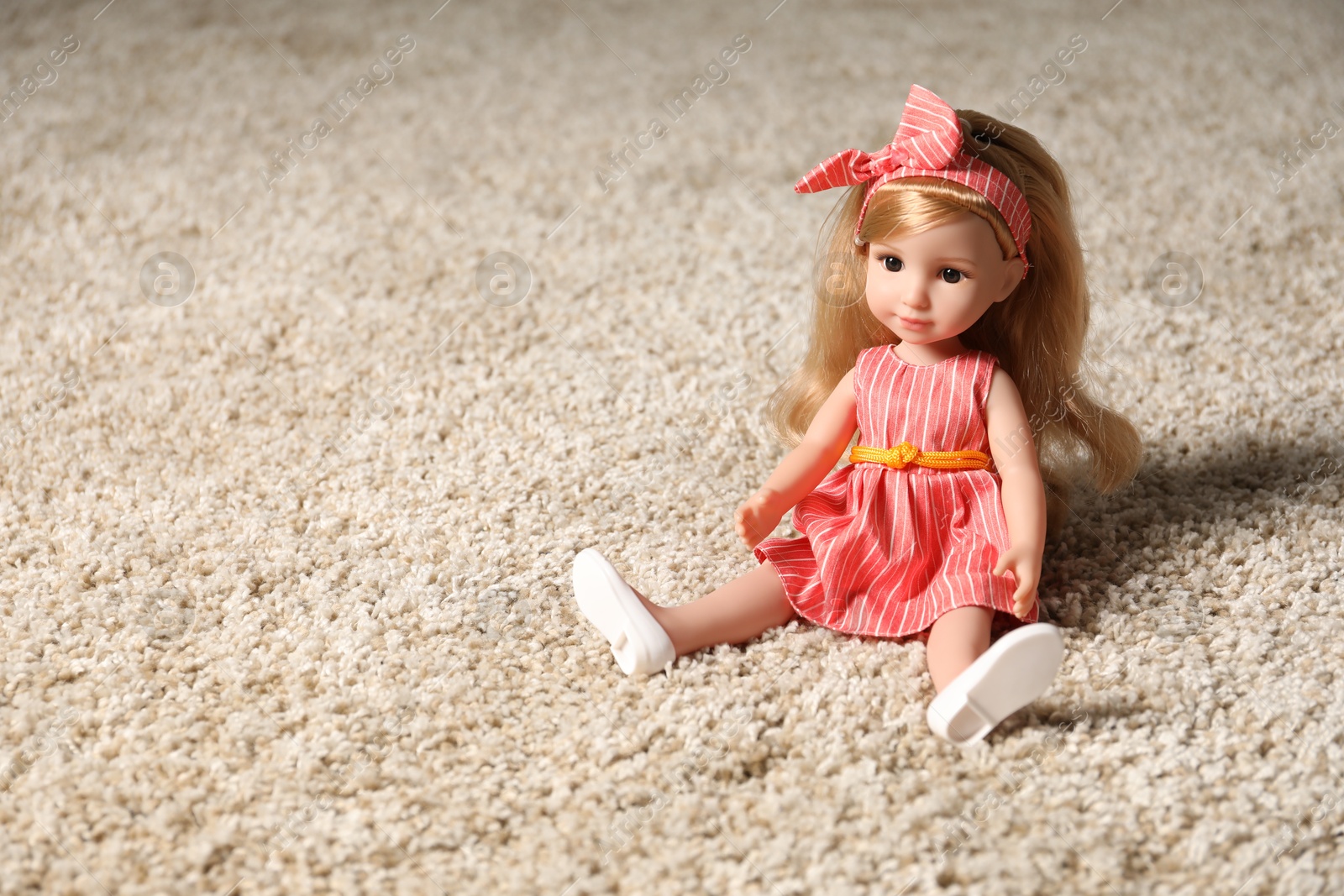 Photo of Beautiful doll in dress and headband on soft carpet. Space for text