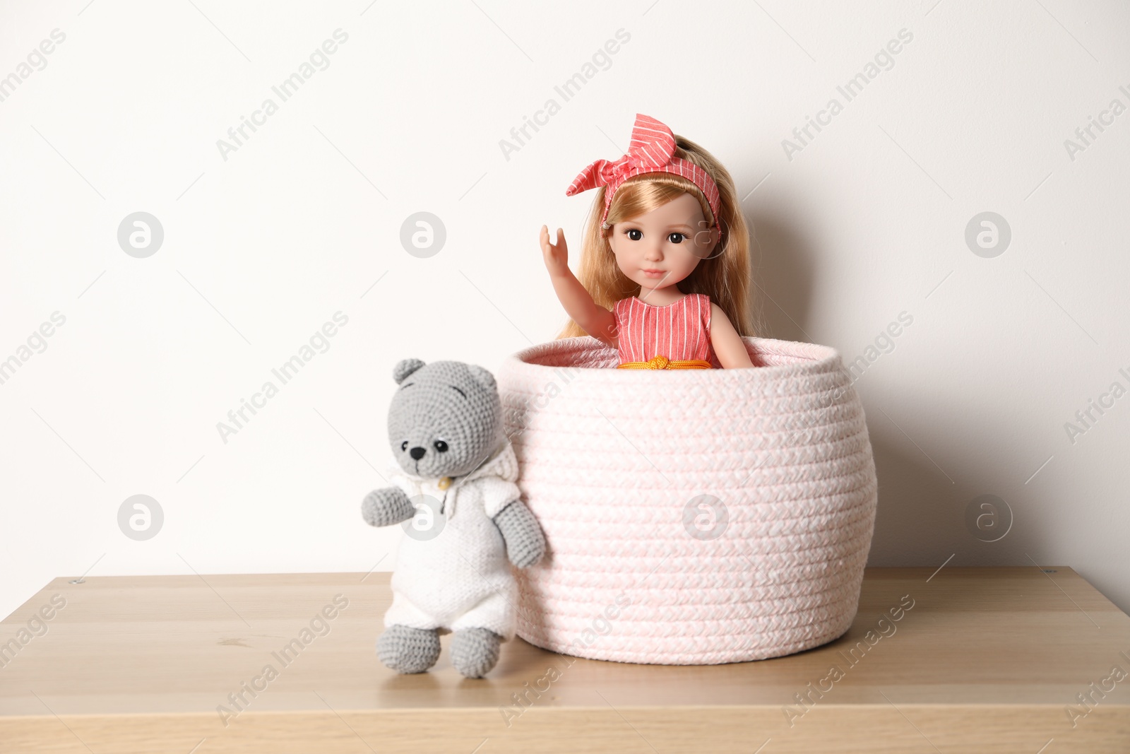 Photo of Beautiful doll and toy bear on wooden table near white wall