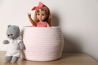 Photo of Beautiful doll and toy bear on wooden table near white wall. Space for text