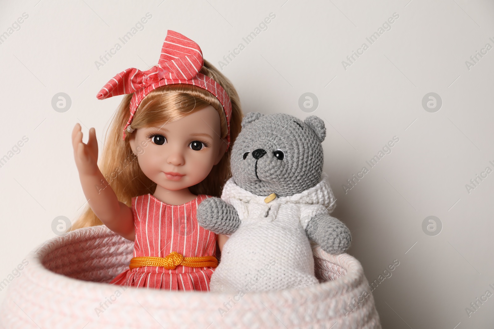 Photo of Beautiful doll and toy bear in basket near white wall, closeup. Space for text