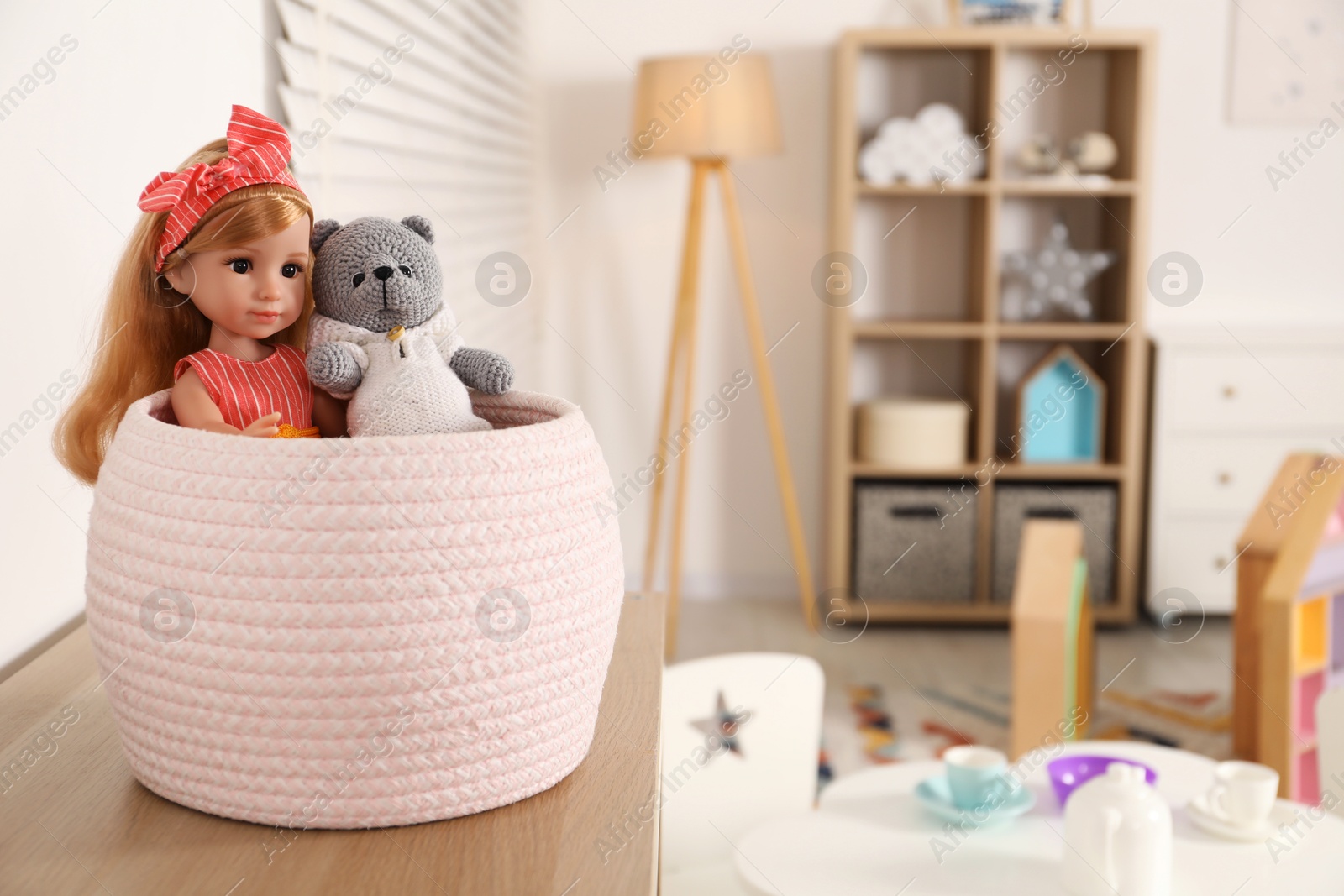 Photo of Beautiful doll and toy bear in basket indoors. Space for text