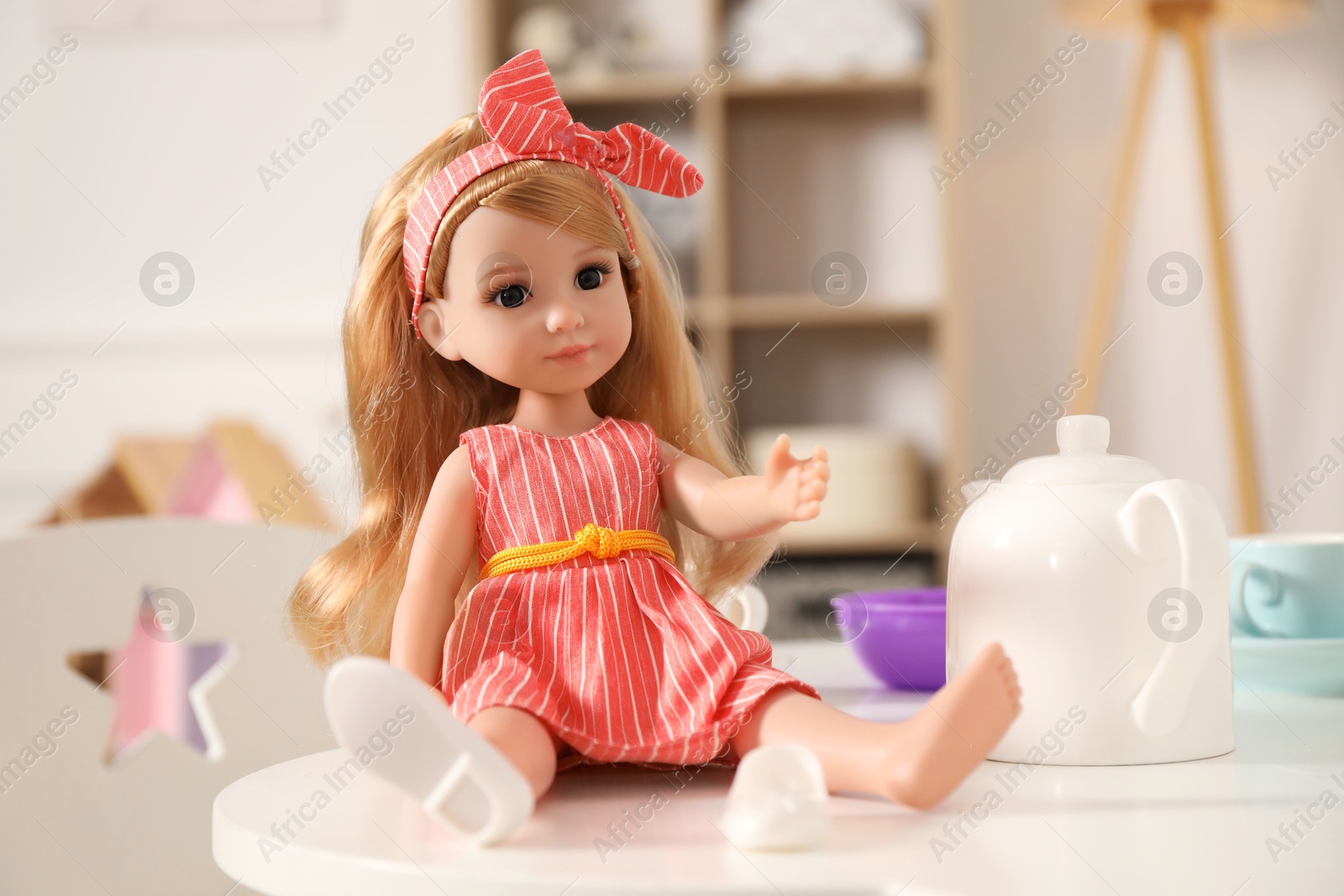 Photo of Beautiful doll and toy dishware on white table indoors