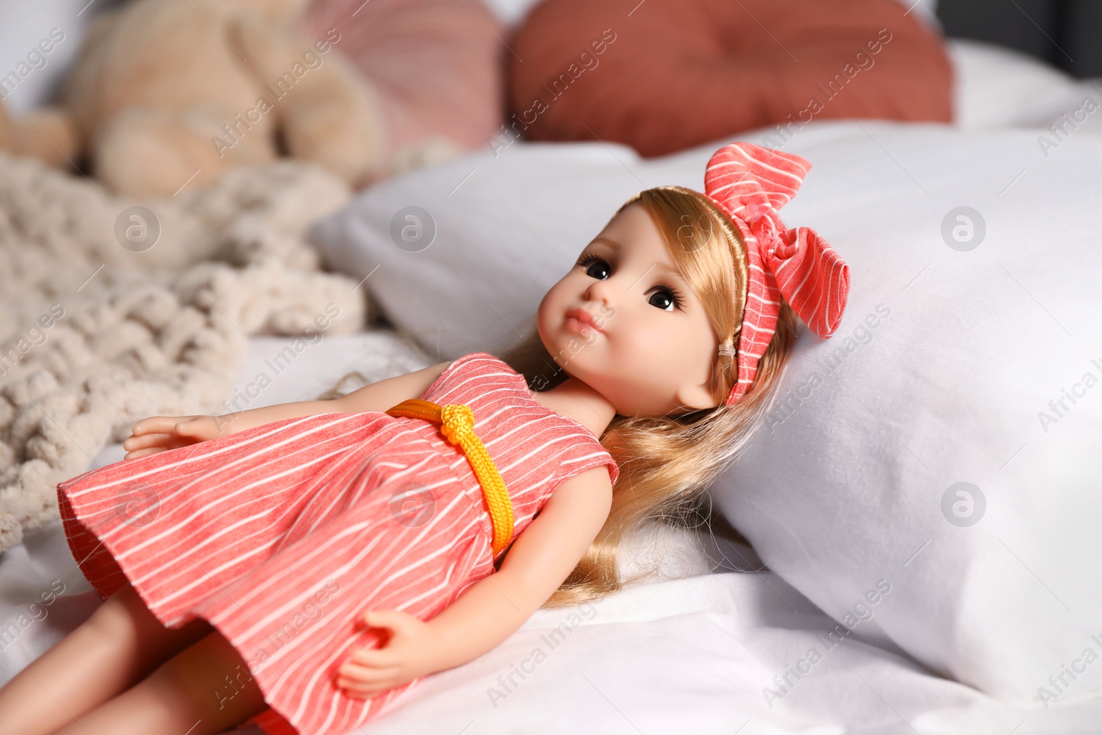 Photo of Beautiful doll in dress and headband on bed, closeup