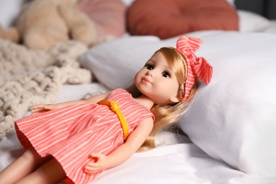 Photo of Beautiful doll in dress and headband on bed, closeup