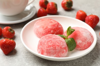 Photo of Delicious mochi, strawberries and mint on gray textured table, closeup