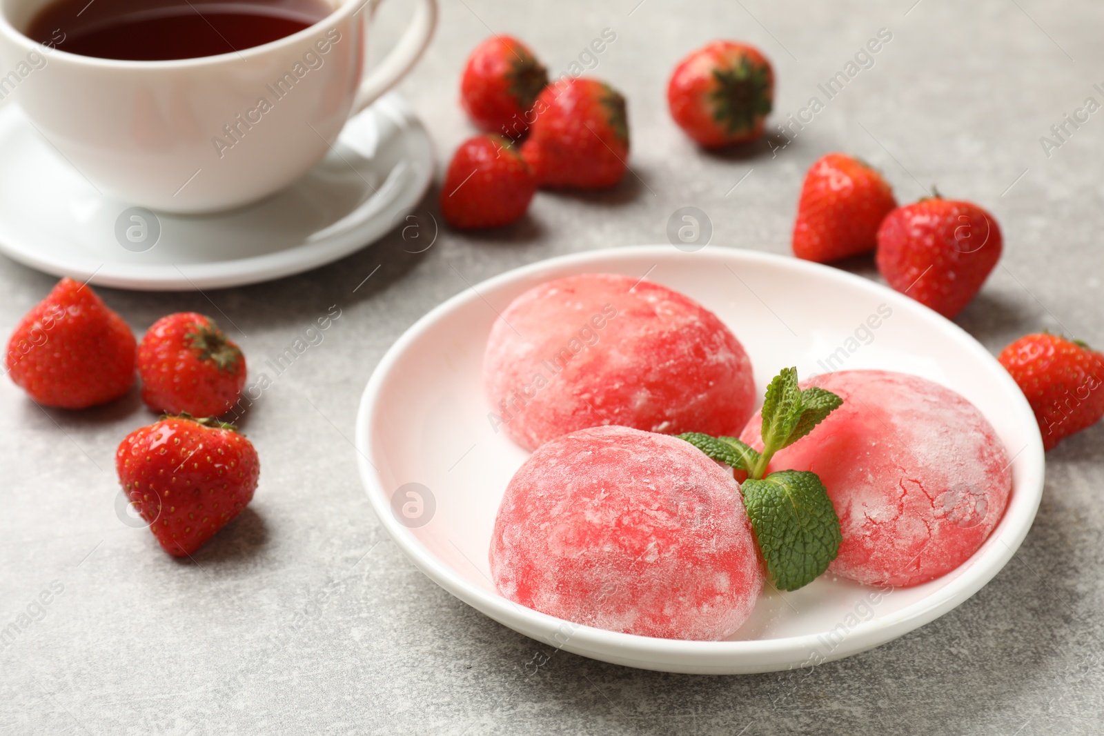 Photo of Delicious mochi, strawberries, mint and tea on gray textured table, closeup