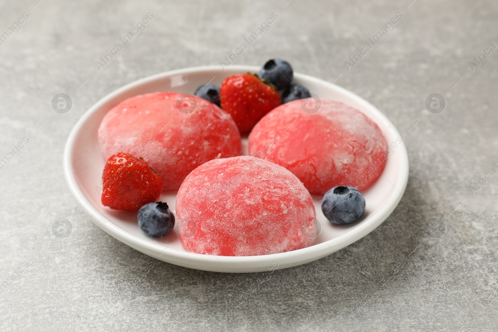 Photo of Delicious mochi, strawberries and blueberries on gray textured table, closeup