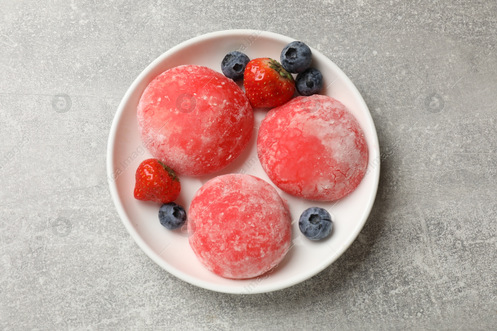 Photo of Delicious mochi, strawberries and blueberries on gray textured table, top view