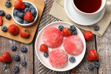 Photo of Delicious mochi, strawberries, blueberries and tea on wooden table, flat lay